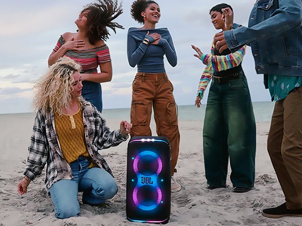 People dancing around a JBL PartyBox on the beach.