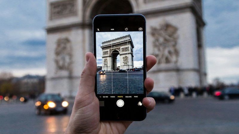 a person holding an iphone taking a photo of the arc de triomphe in paris