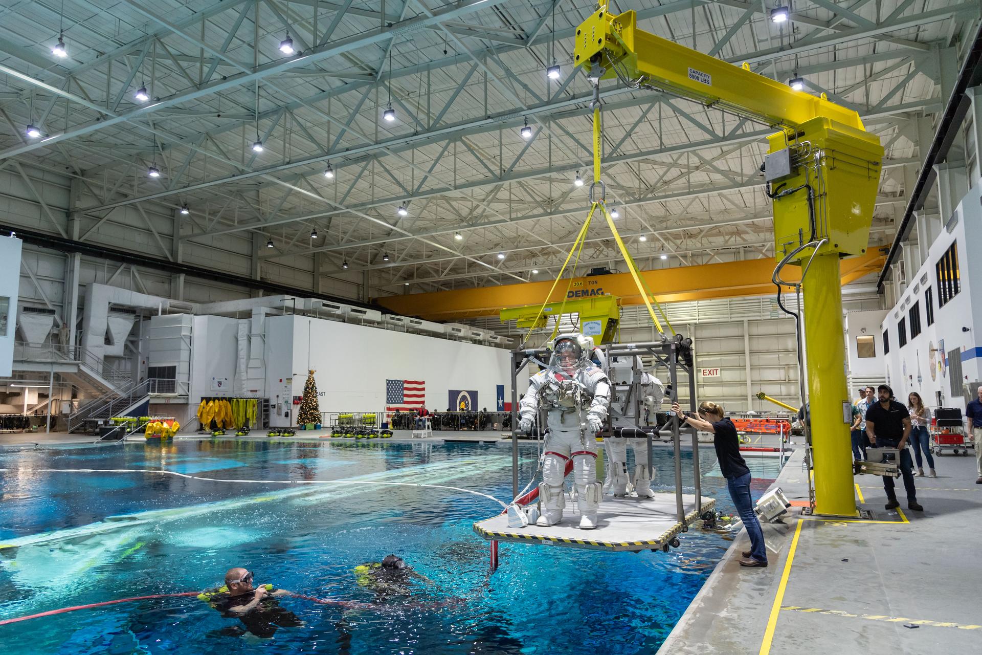 een astronaut staat op een platform dat op het punt staat in een groot zwembad te worden neergelaten