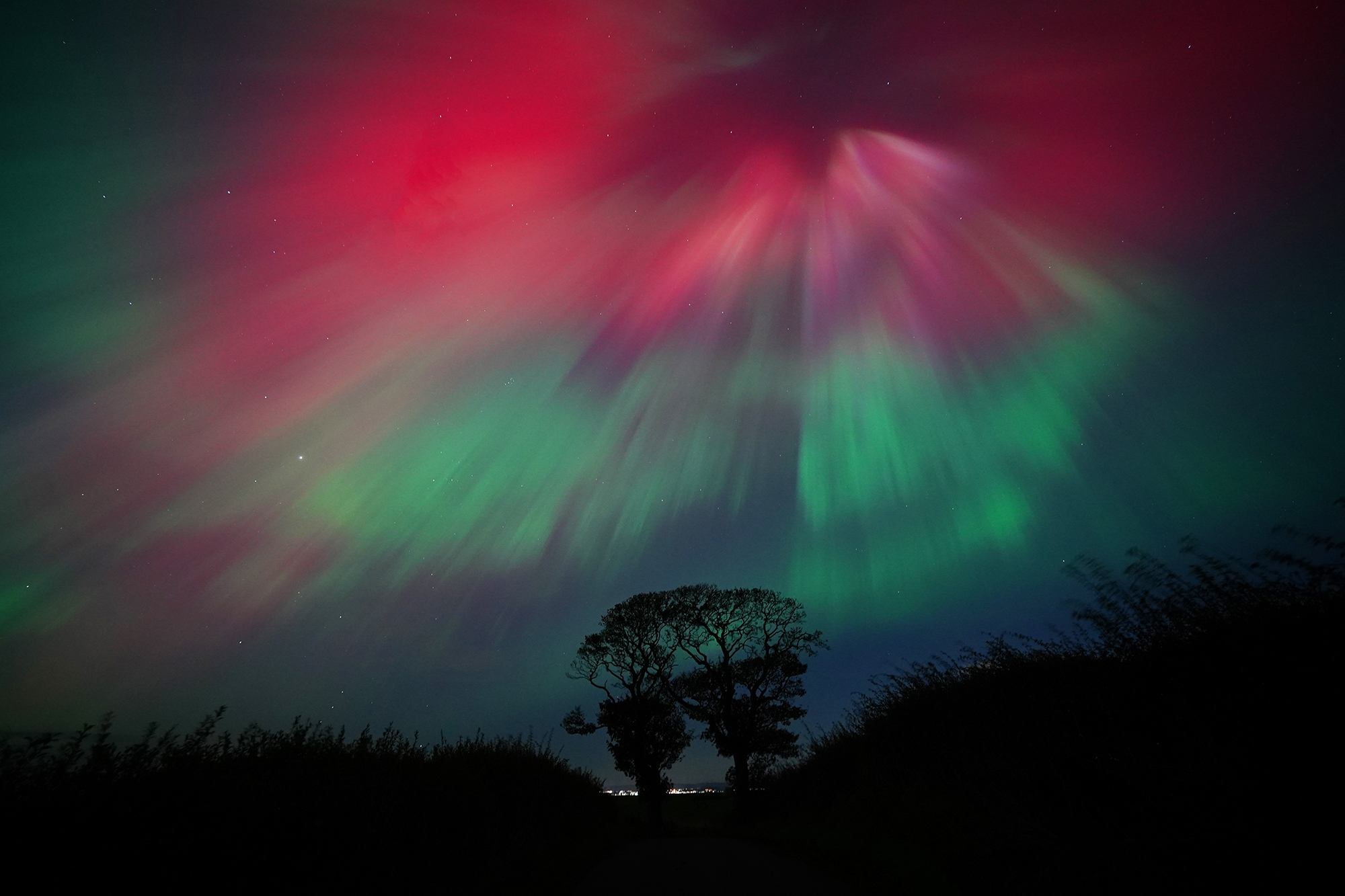 The Northern Lights, also known as the aurora borealis, on display in the skies above The Kissing Trees near Kinghorn in Fife. Aurora displays occur when charged particles collide with gases in the Earth's atmosphere around the magnetic poles. As they collide, light is emitted at various wavelengths, creating colourful displays in the sky. Picture date: Friday October 11, 2024. (Photo by Jane Barlow/PA Images via Getty Images)