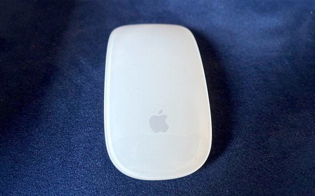 A white Apple Magic Mouse on a blue couch cushion