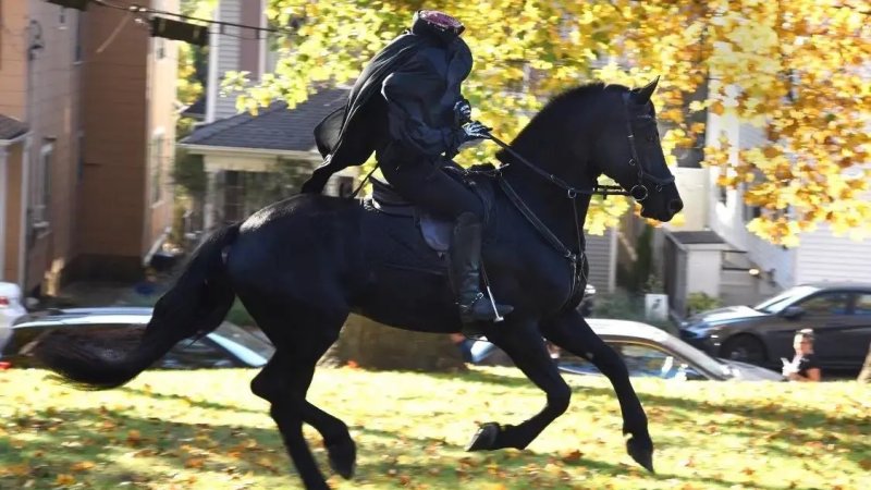 a rider in a headless horseman costume rides by yellow fall leaves