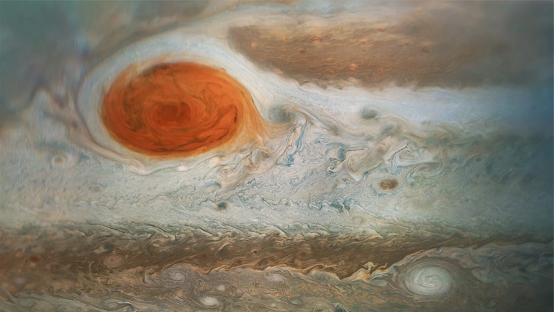 a close-up of the planet jupiter's great red spot. it is a swirling red storm on the planet's more white and orange surface