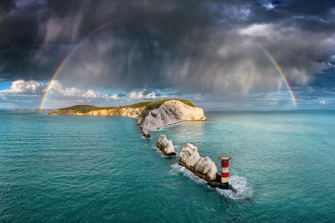 storm clouds and a rainbow form over narrow islands. a lighthouse