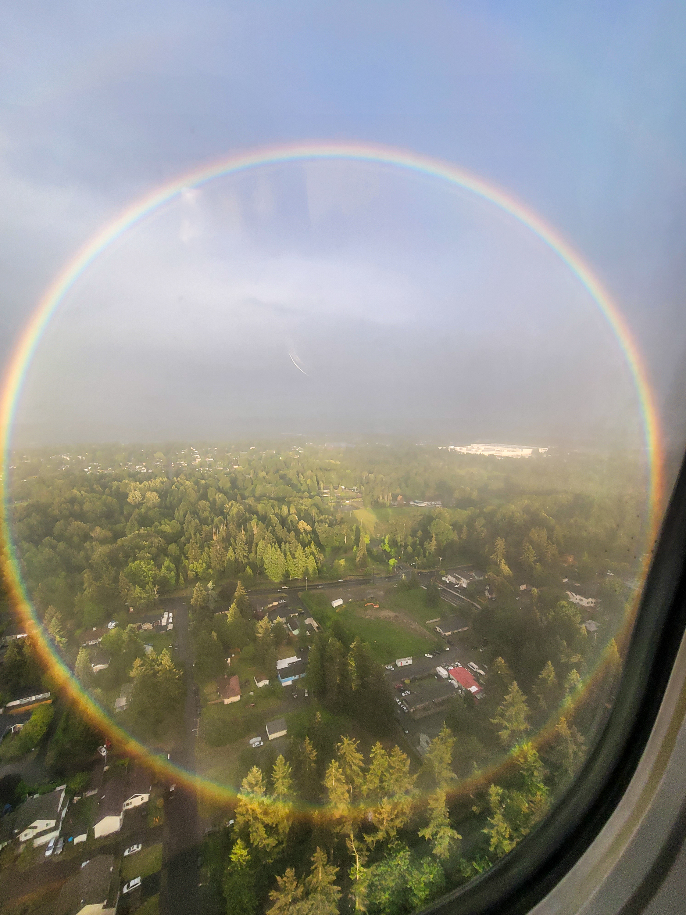 a circular rainbow seen out the window of an airplane over green area