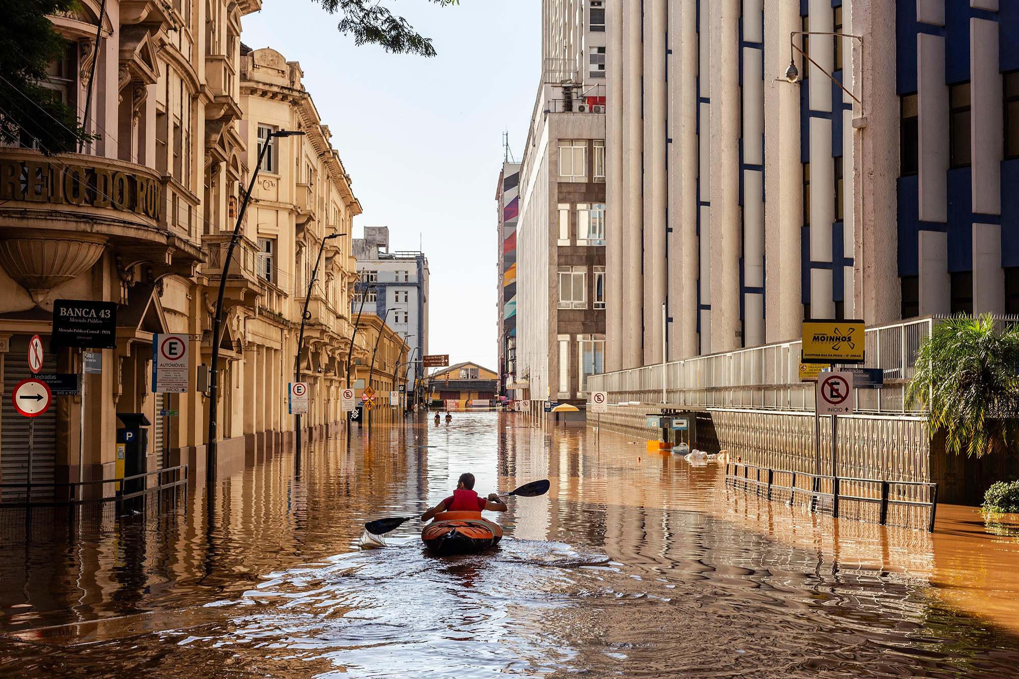 a kayaker in the middle of a flooded street with buildings on either side