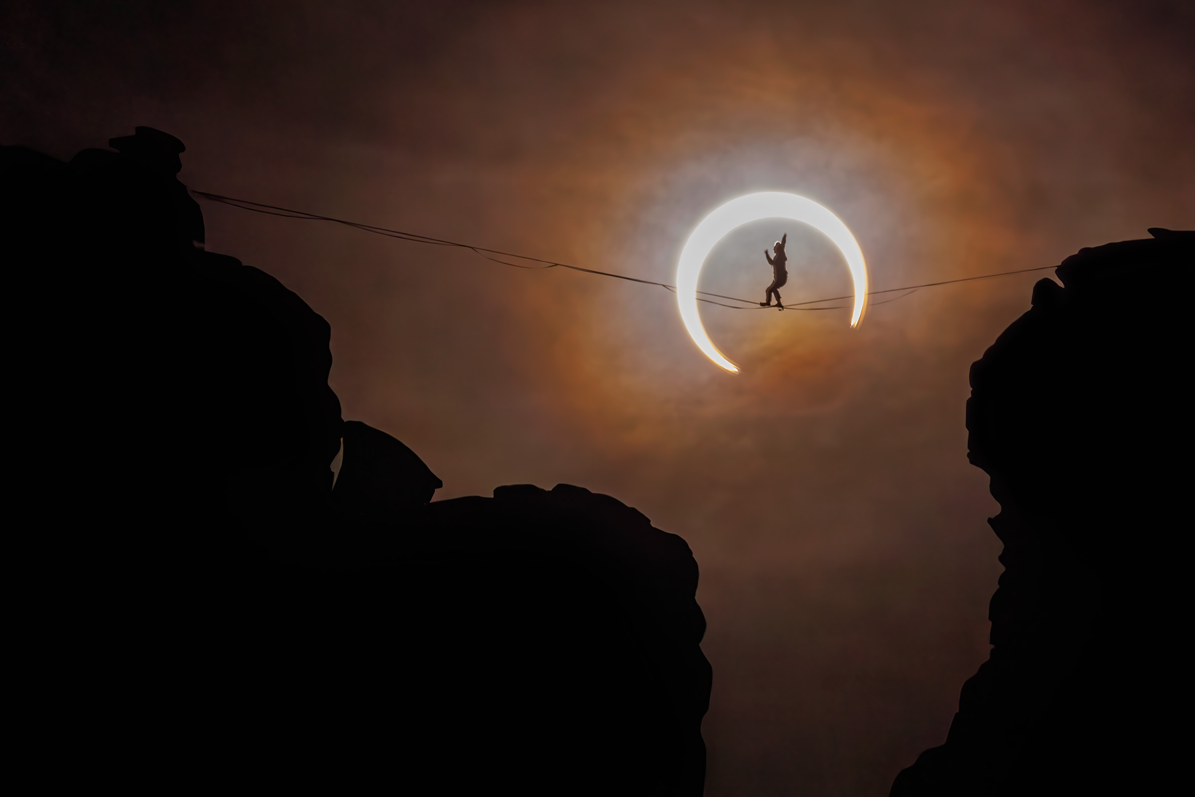 a person on a tightrope walks in front of the solar eclipse. a crescent of the sun shows