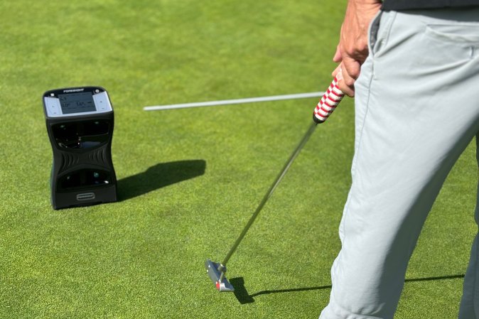 A golder on the green swinging a putter in front of a Foresight Sports QuadMax portable gold launch monitor