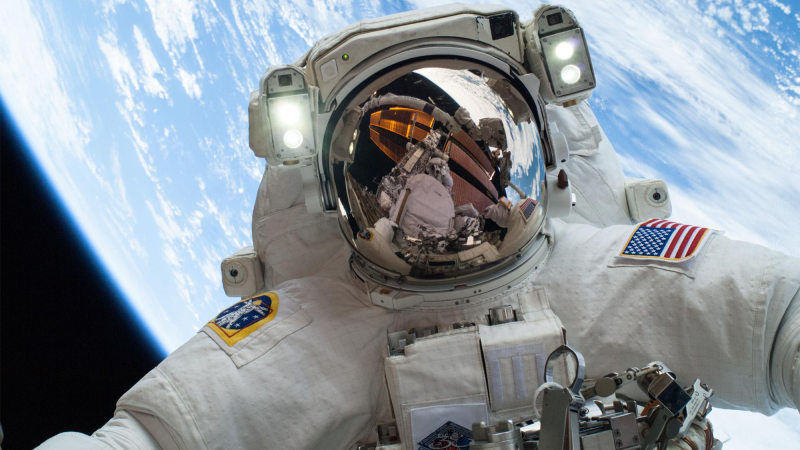 an astronaut on a spacewalk in a full spacesuit takes a selfie with earth in the background