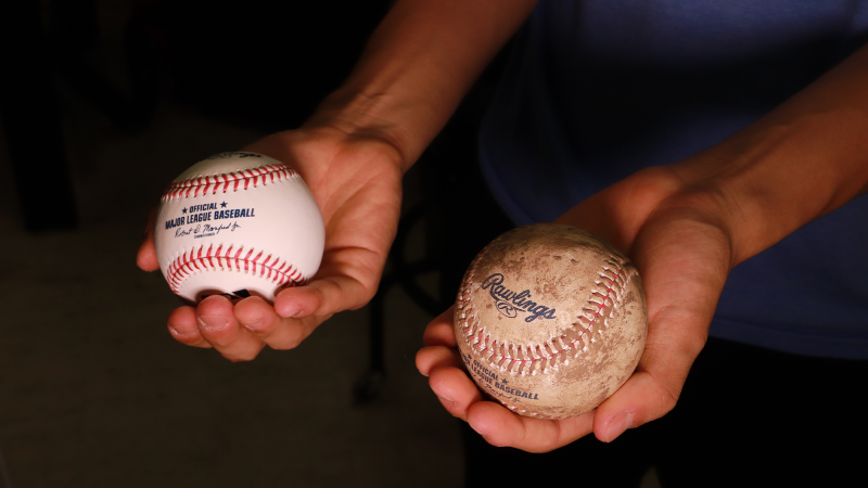 two baseballs held in two hands. one is bright white and the other is coated with a brown mud