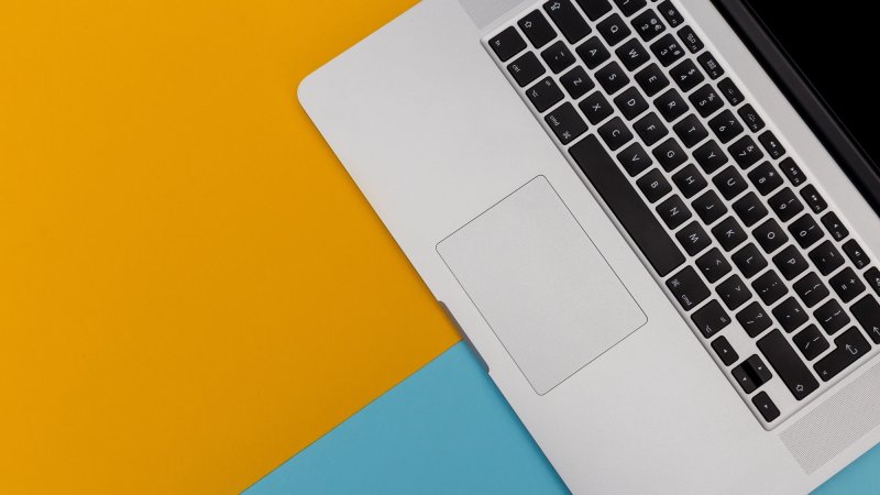 Laptop computer keyboard overhead on bright yellow and blue background with copy space