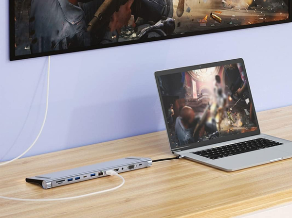 A laptop plugged into a hub sitting on a desk.