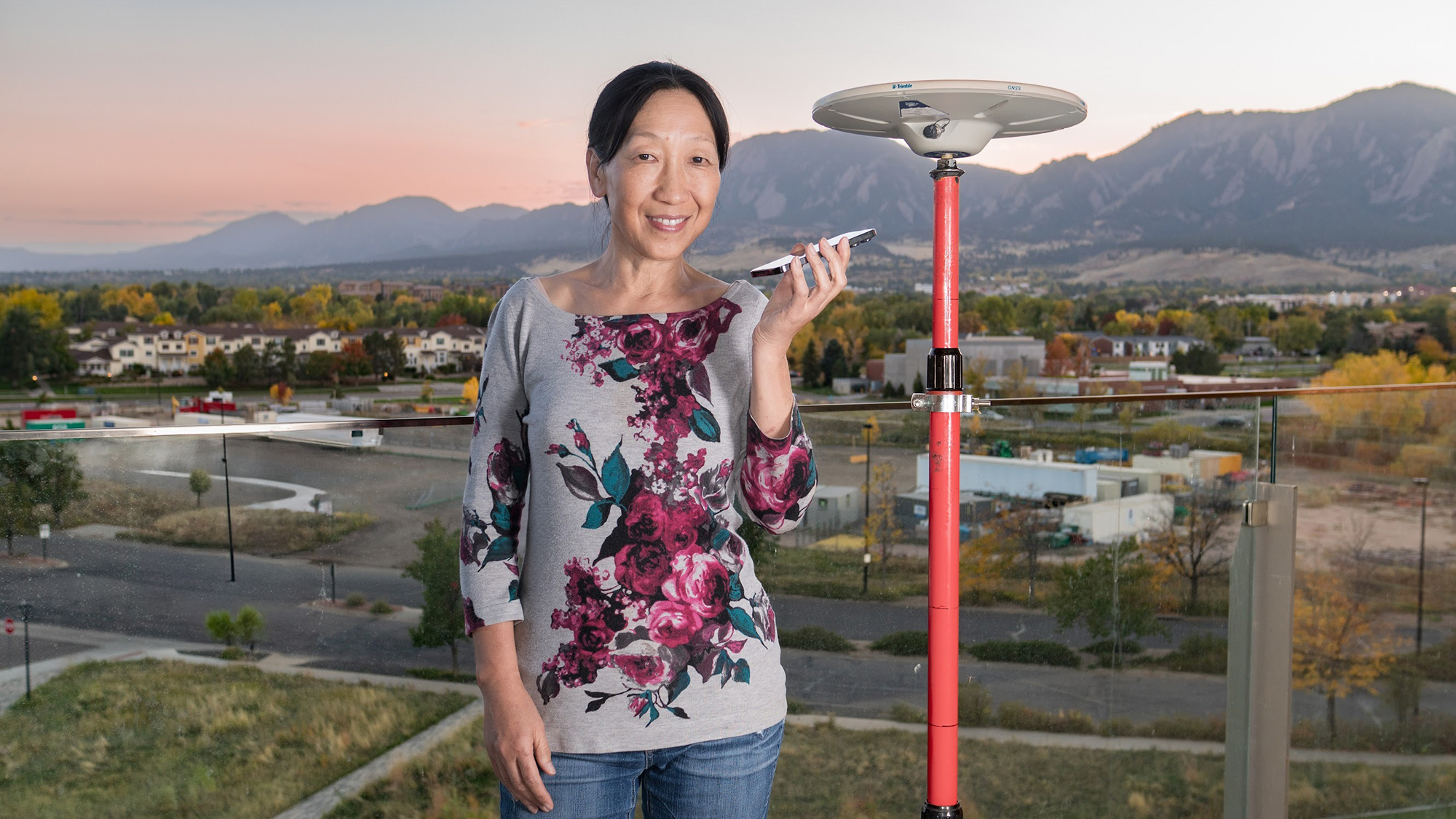 Professor Jade Morton (co-author) posing with a phone and a monitoring station at the University of Colorado, Boulder. A monitoring station has a large and expensive antenna. Phones have smaller antennas, which leads to noisier measurements, but phones are present in more parts of the world.