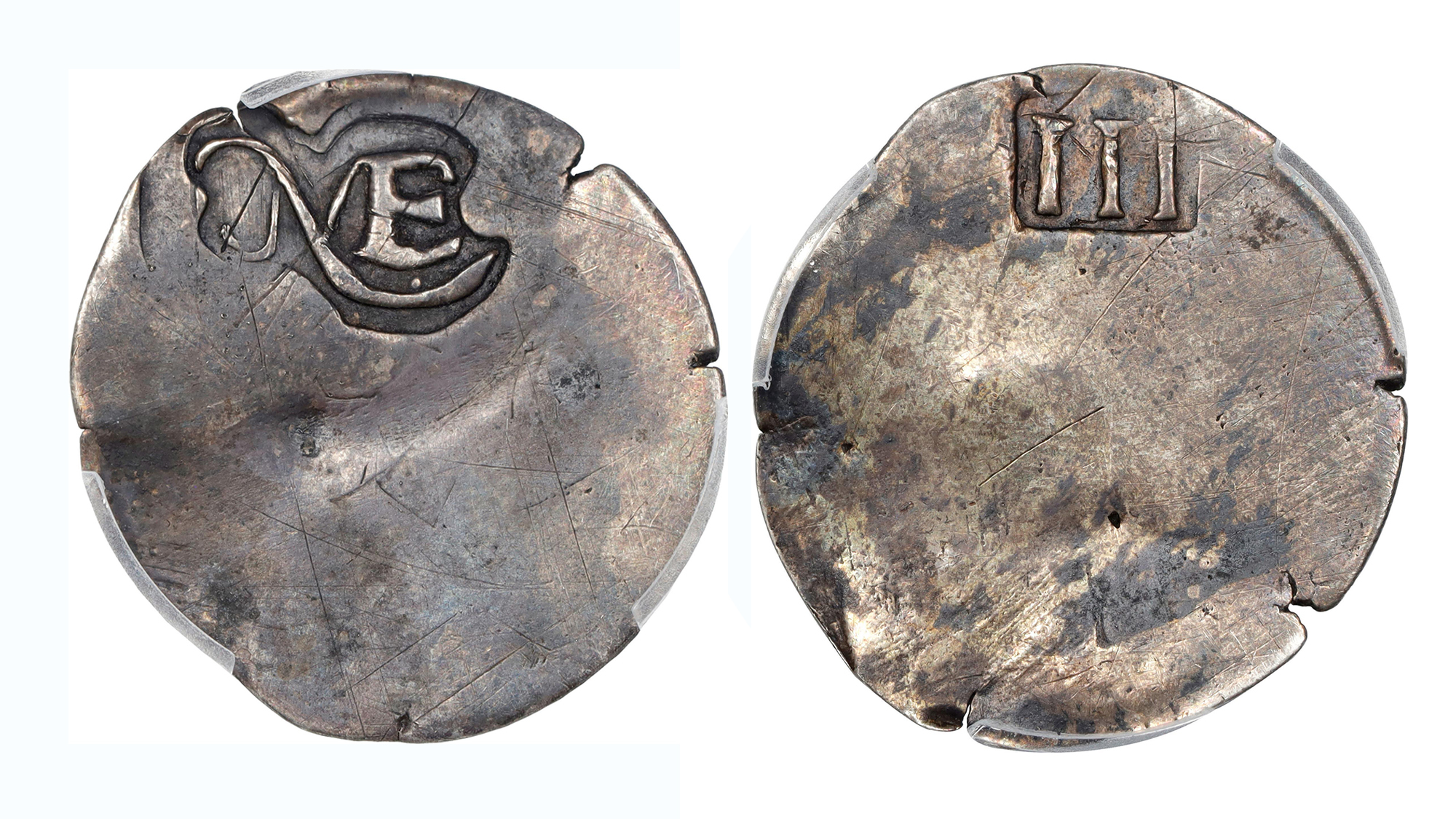 a silver coin minted before the american revolution. one side has the letters NE on it for new england and the other has the roman numeral 3 for its value