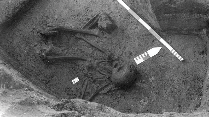 Inhumation grave 26, shown in the original field photograph (left), with bones in anatomical articulation lying on their right side with flexed legs.