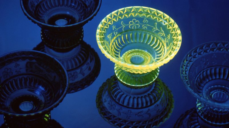 Uranium incorporated for color causes fluorescence under ultraviolet light. A wildflower pattern adorns this 19th century glass bowl. The other bowls are blue, amber, and clear. Centreville, Maryland, USA.