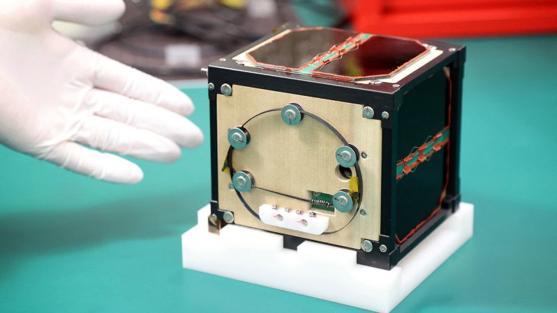 Gloved hand pointing to LignoSat wooden satellite prototype