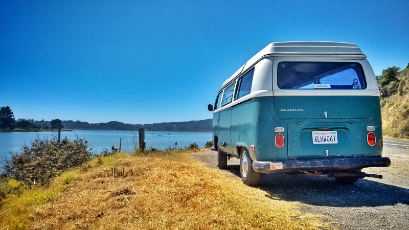 a vintage blue VW van parked at a lake