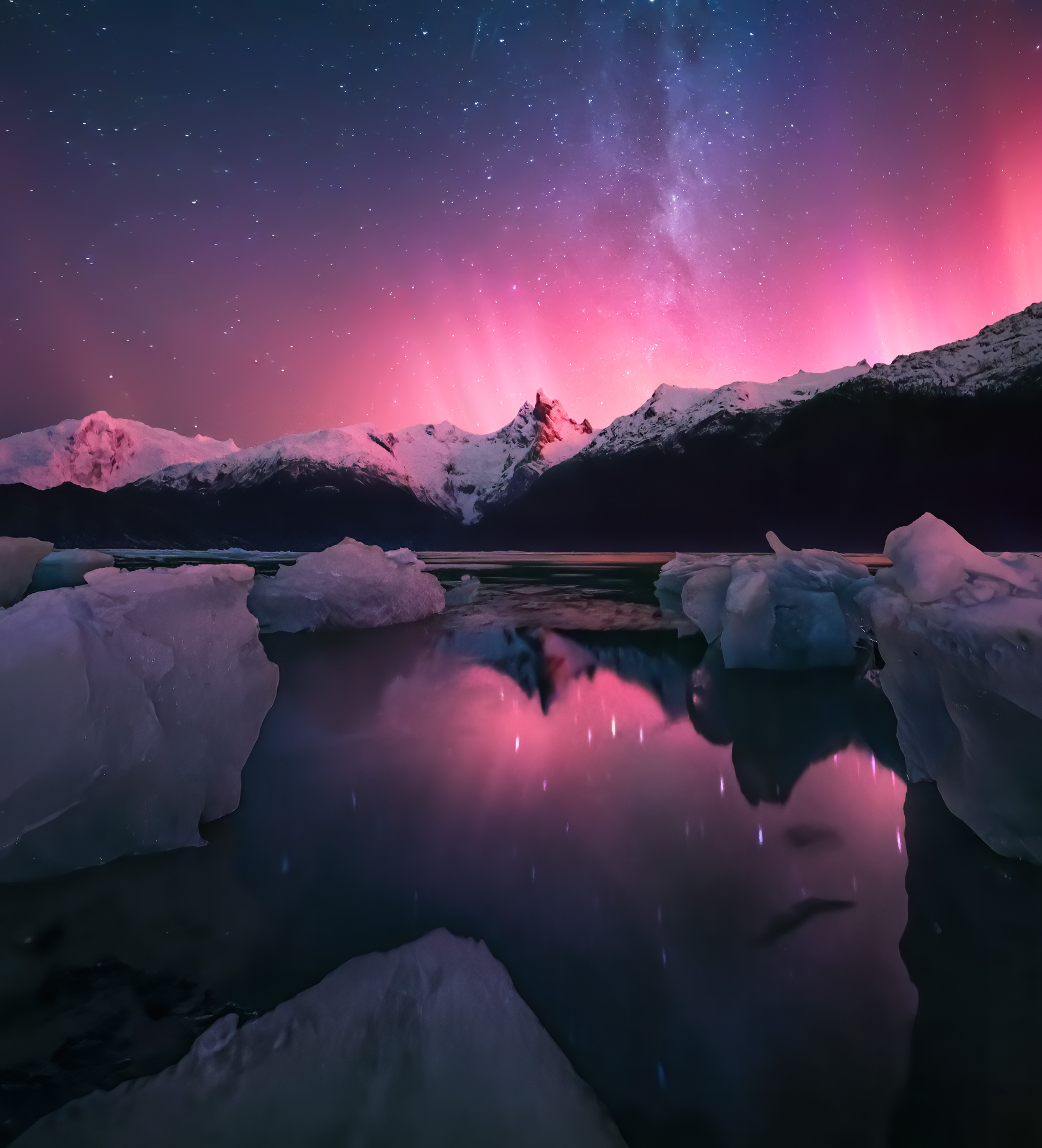 a pink aurora rises behind mountains