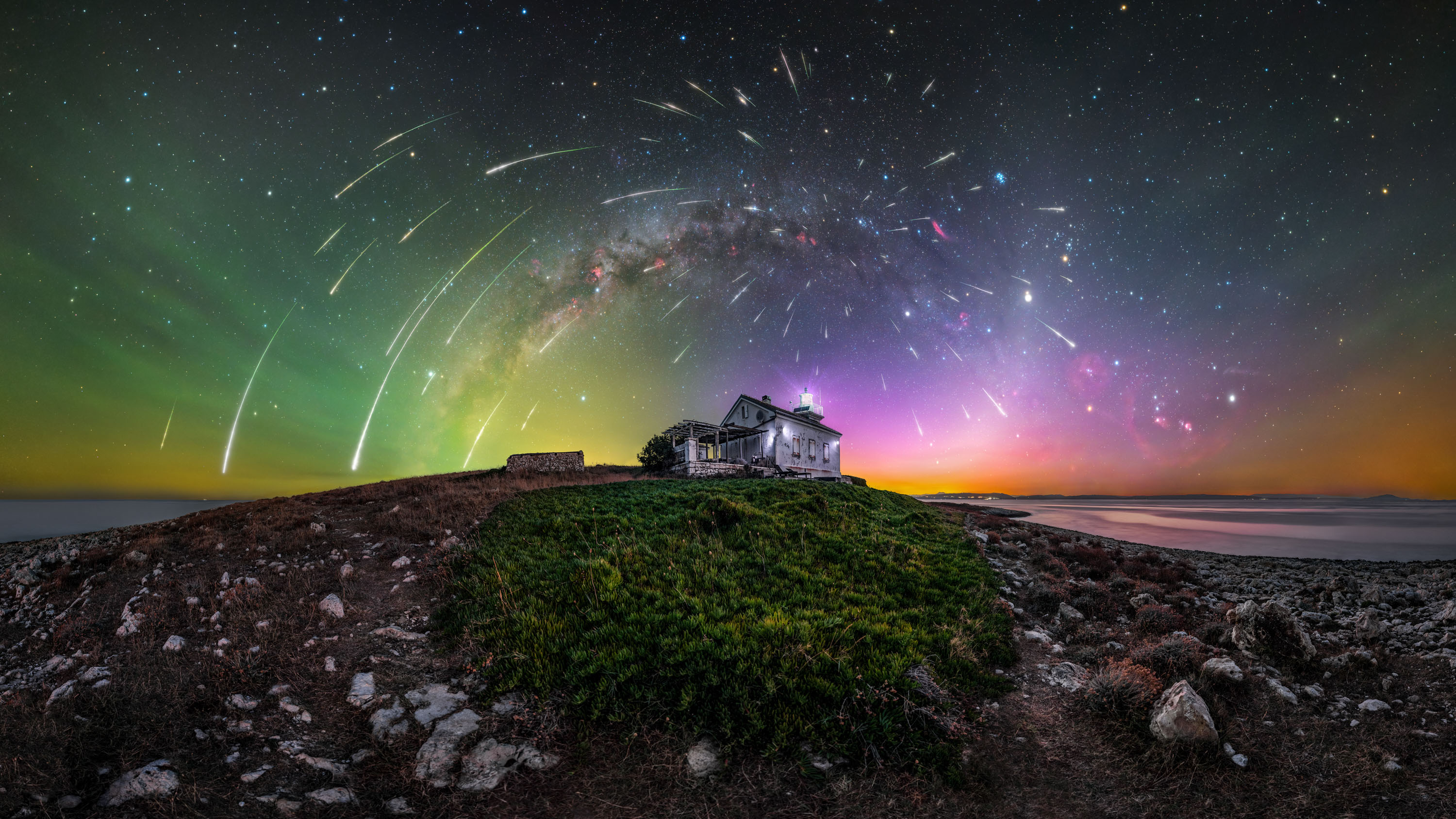 stars look like streaks over a seaside house as the aurora glows on the horizon