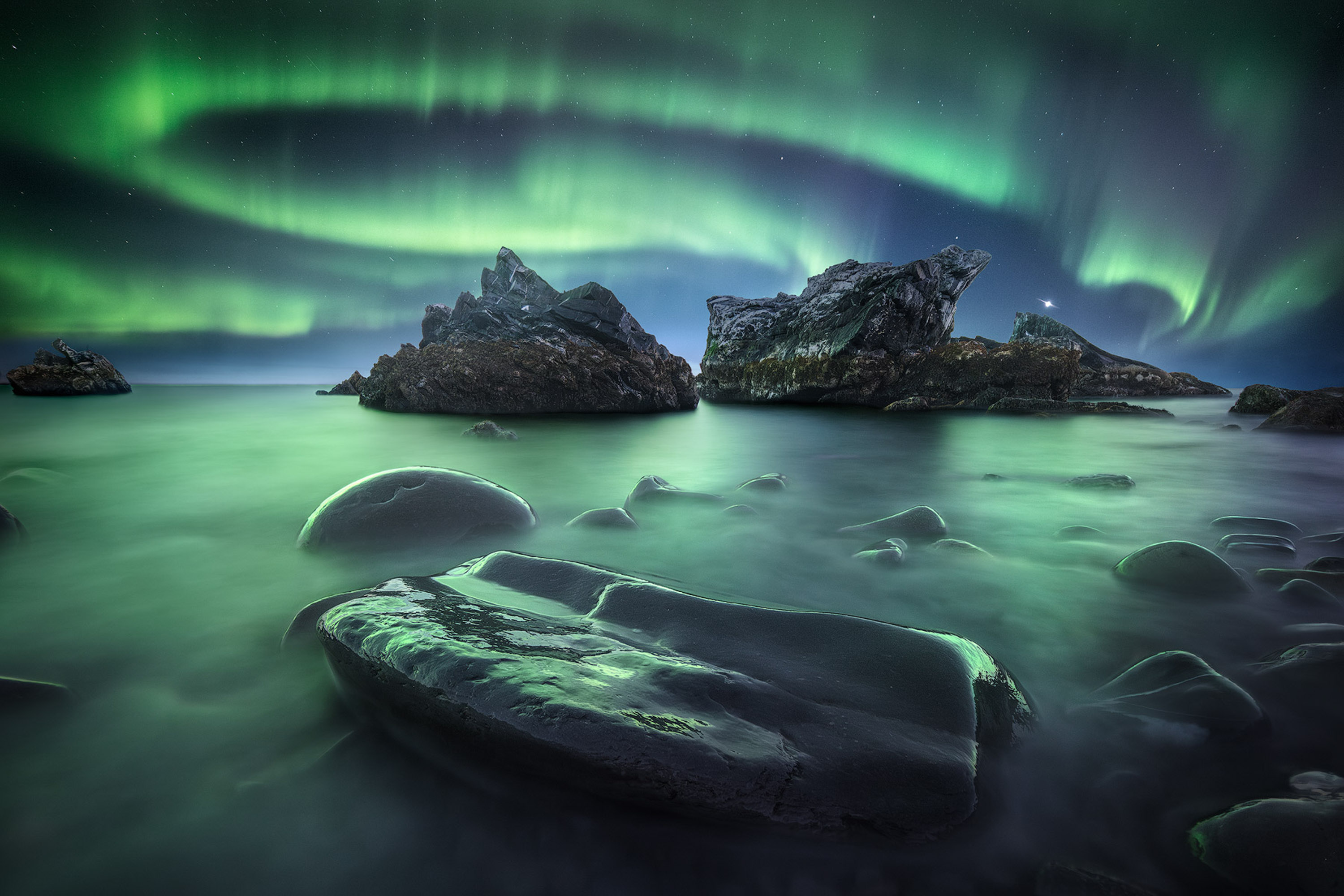 a green aurora streaks across the sky as mist settles on the water and rocks