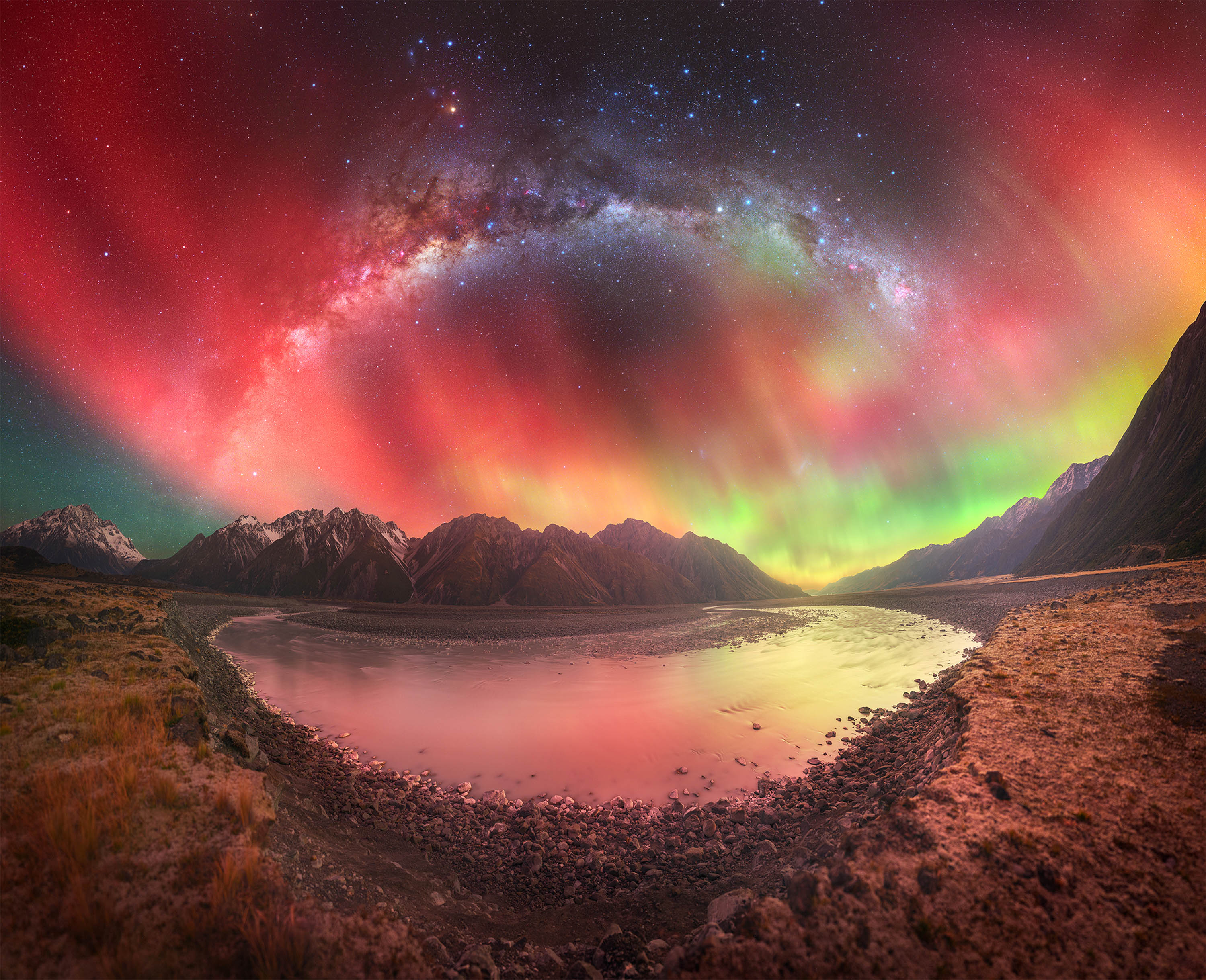 the milky way appears in the middle of an aurora that resembles a fire in rocky terrain