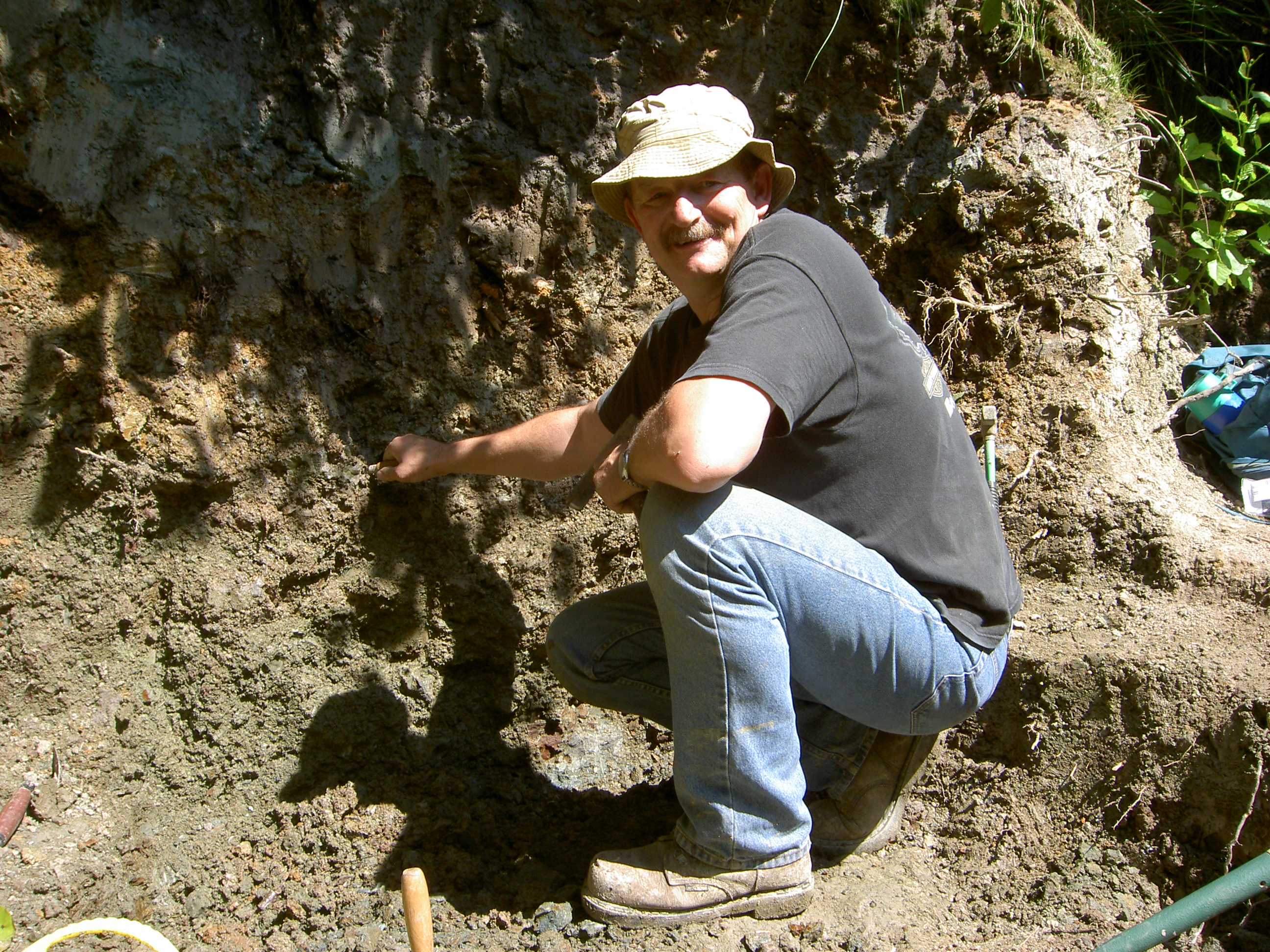 a man crouches down in a dig site showing where he found tyrannosaur teeth