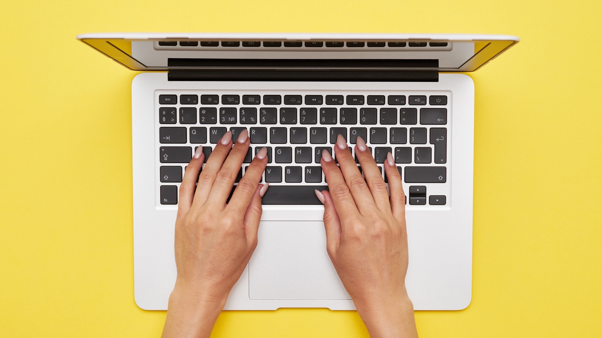 Flat lay of woman hands printing in laptop standing on yellow background