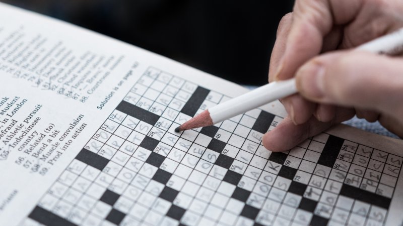 Close up of hand holding pencil solving crossword puzzle