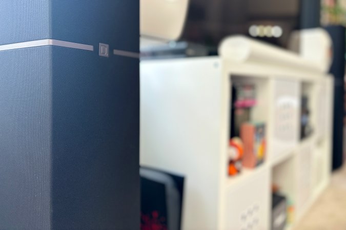  Black Definitive Technology Dymension DM70 speaker in front of a white credenza and a Samsung 8K TV