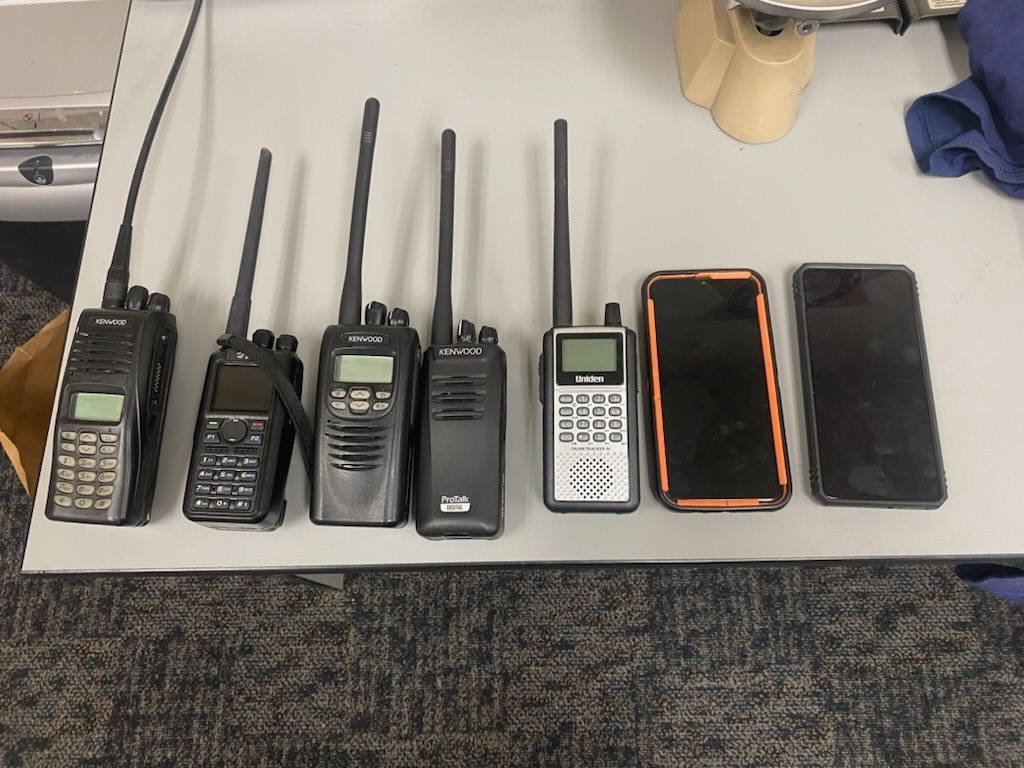 Row of walkie talkies and smart phones on table