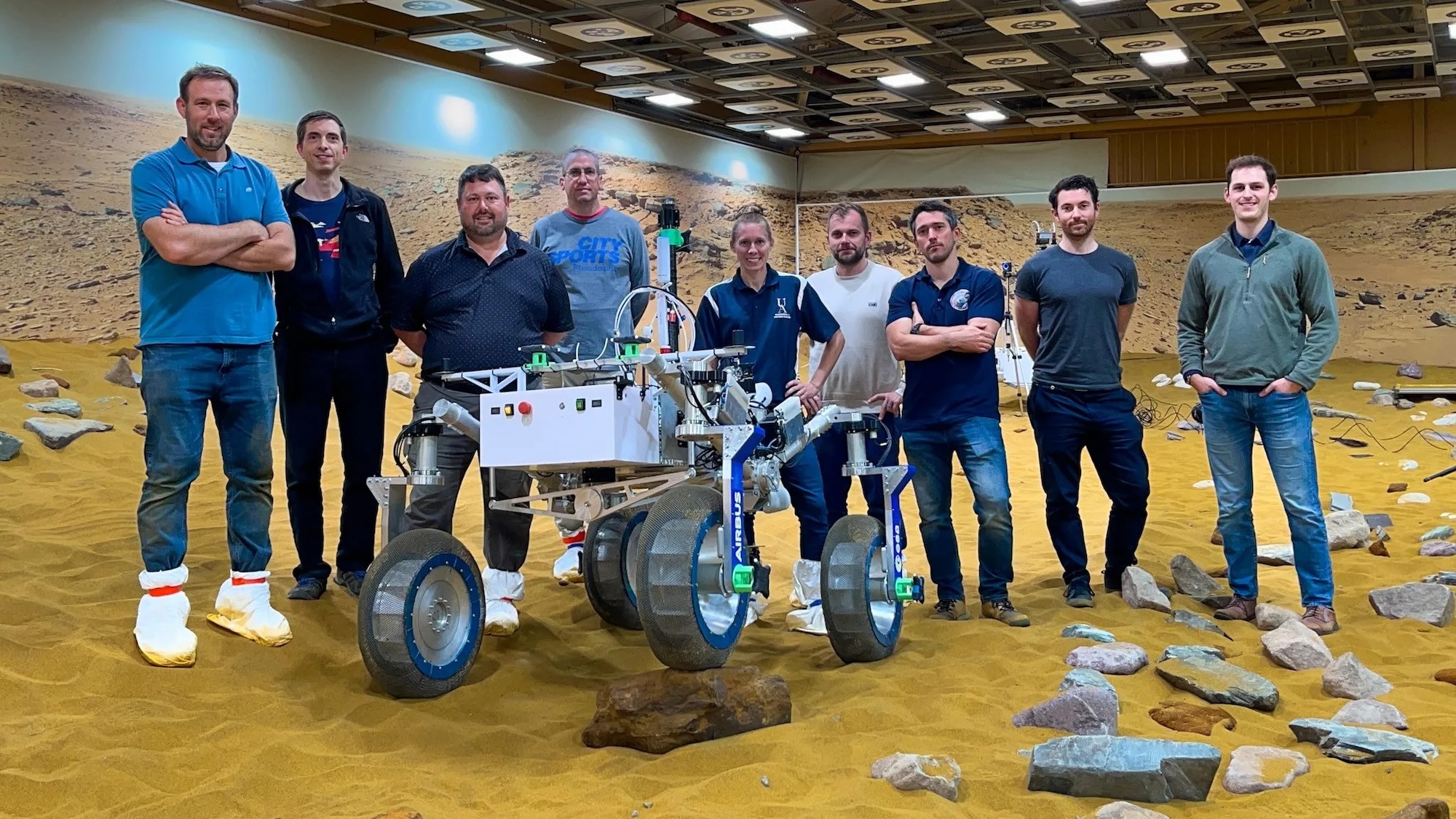 Researchers from NASA’s Glenn Research Center and Airbus Defence & Space pose with a test rover on Martian-simulated terrain.