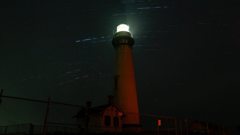 meteors fall in the night sky near a lighthouse