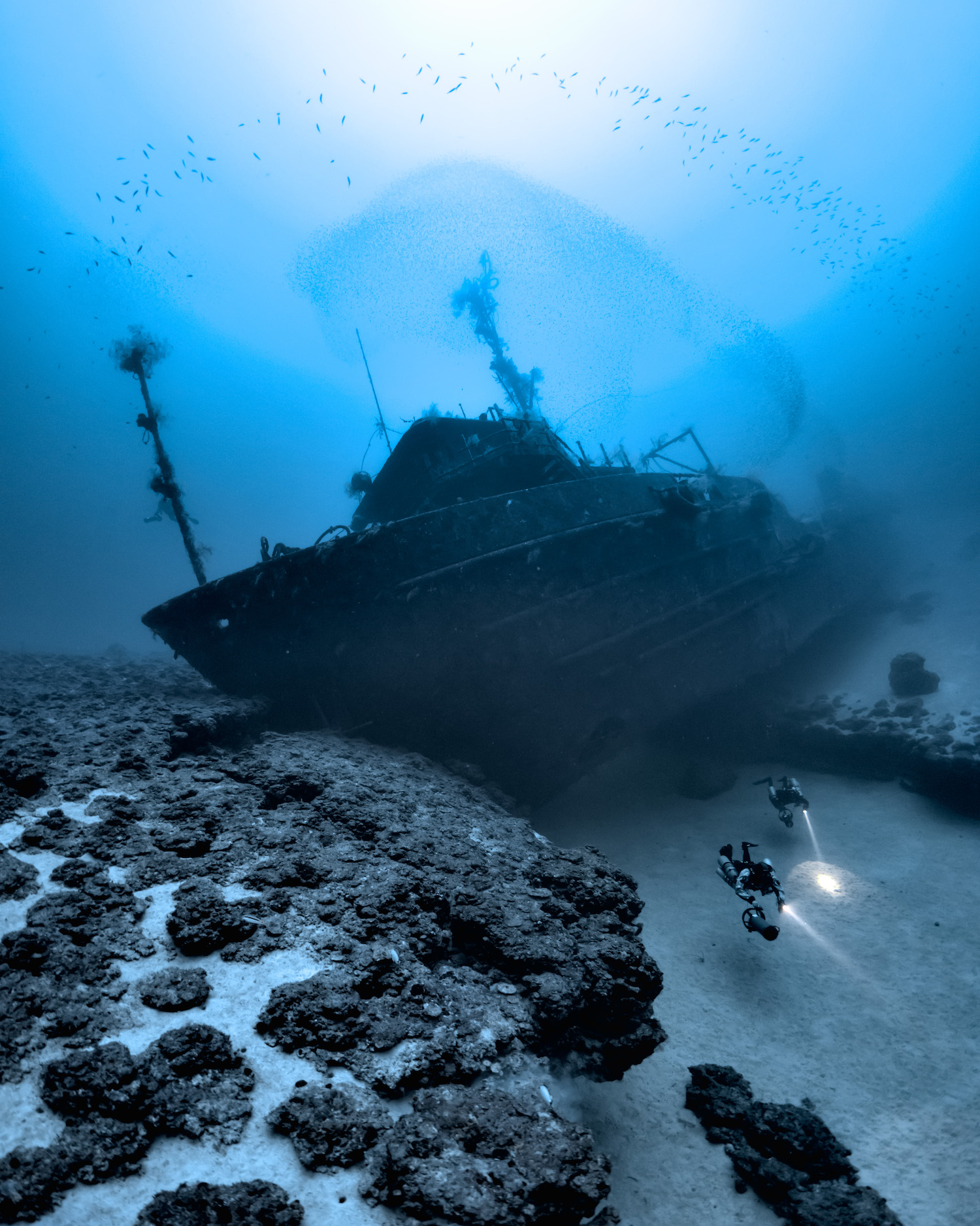 a large ship on the ocean floor. two divers with lights nearby