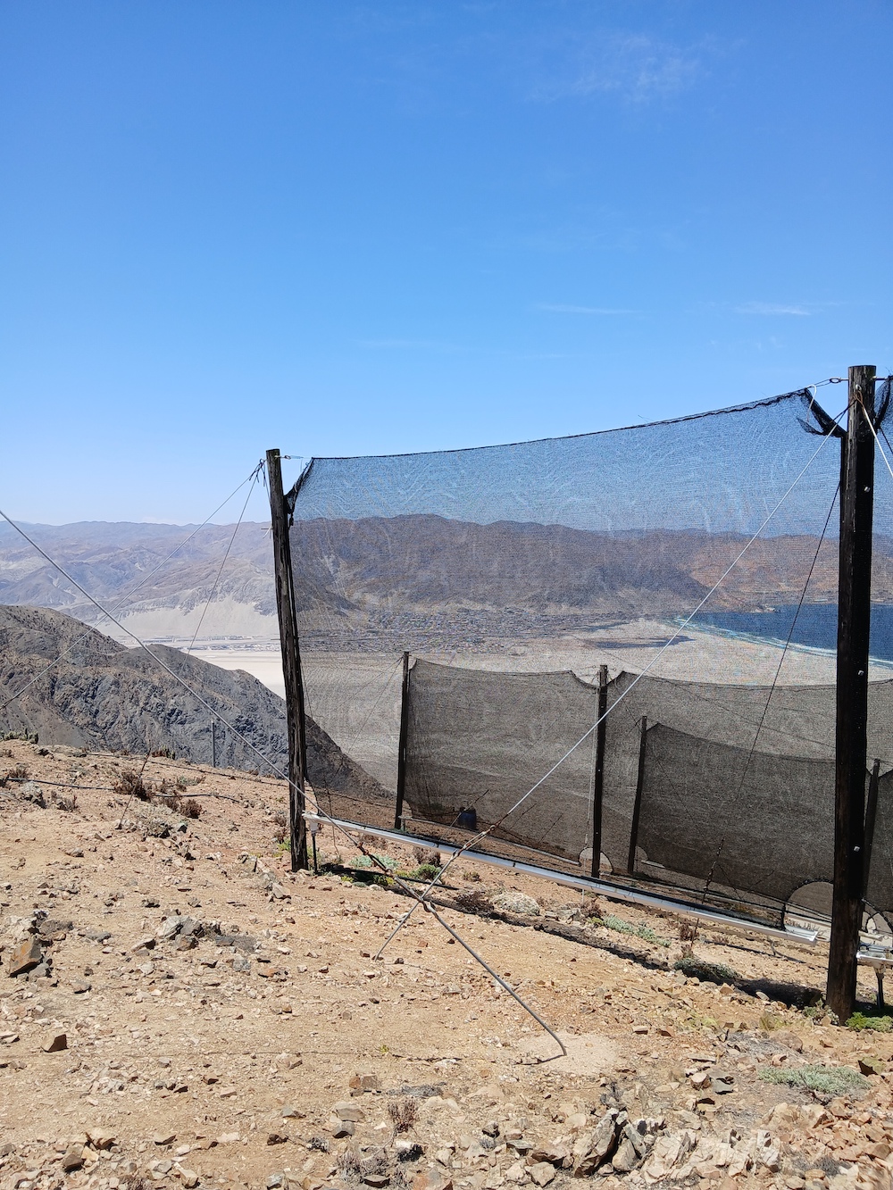 mesh panels on a desert hill side. the ocean is seen in the background