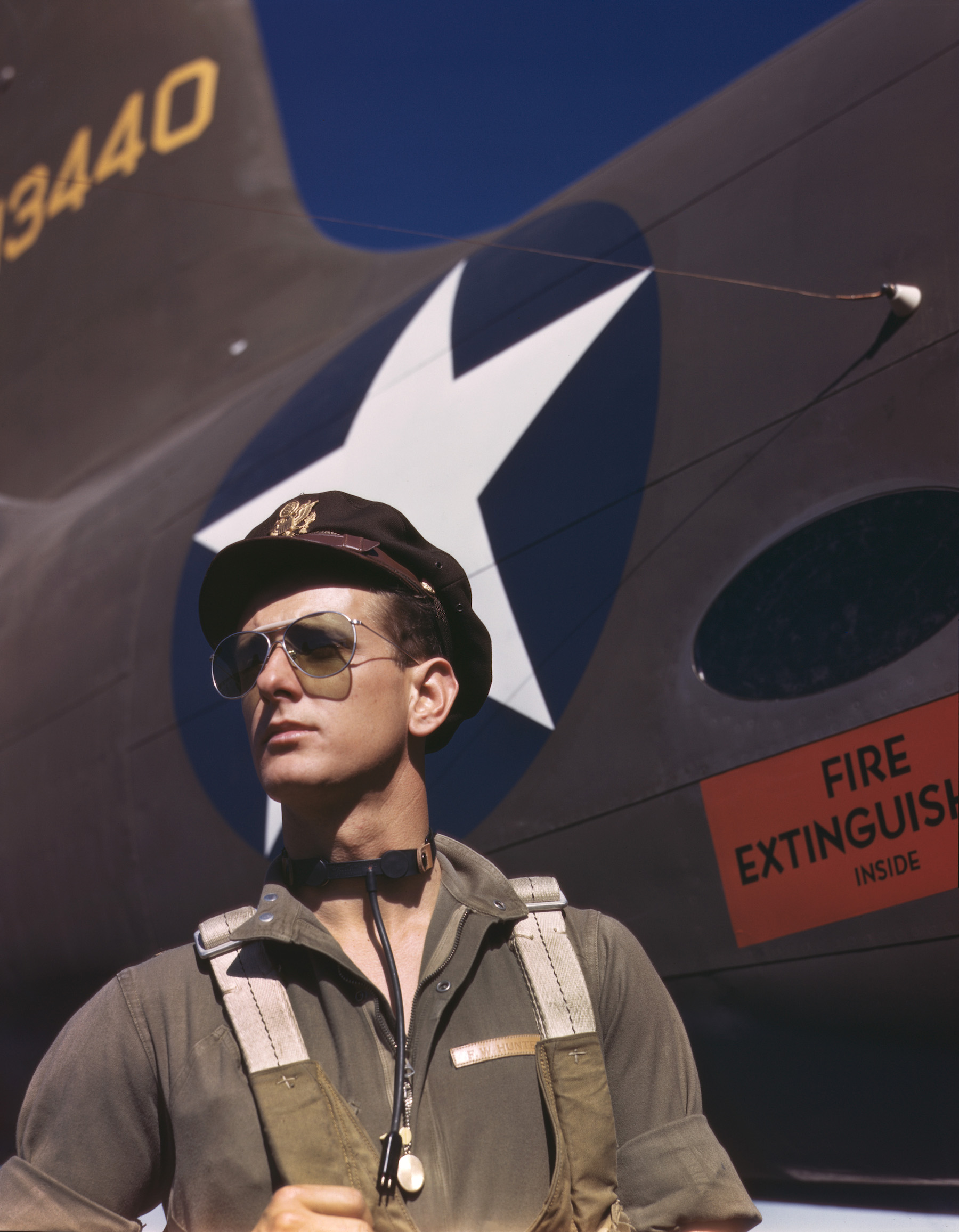 -a test pilot stands in from of an airplane in his uniform wearing aviator sunglasses