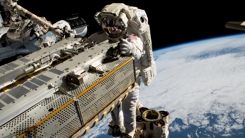 an astronaut performs a space walk on the international space station. earth is visible in the foreground.