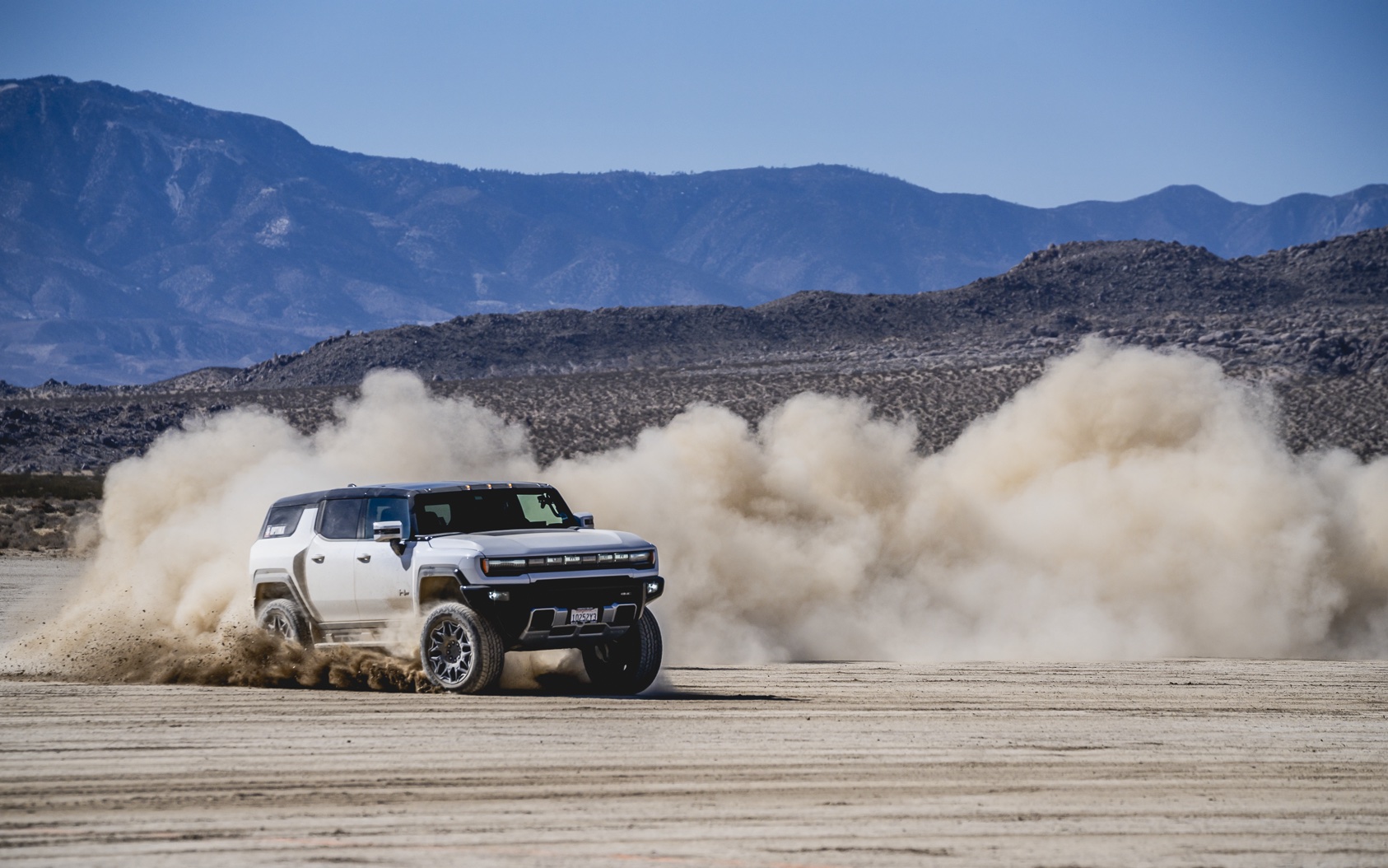 a hummer SUV rips across the sand and dirt, kicking up a cloud of dust