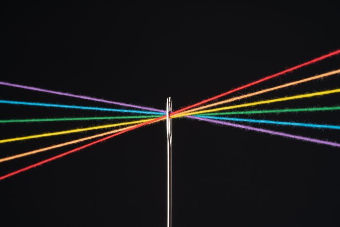 Rainbow Colored Threads Through Needle Eyelet Against Black Colored Background.