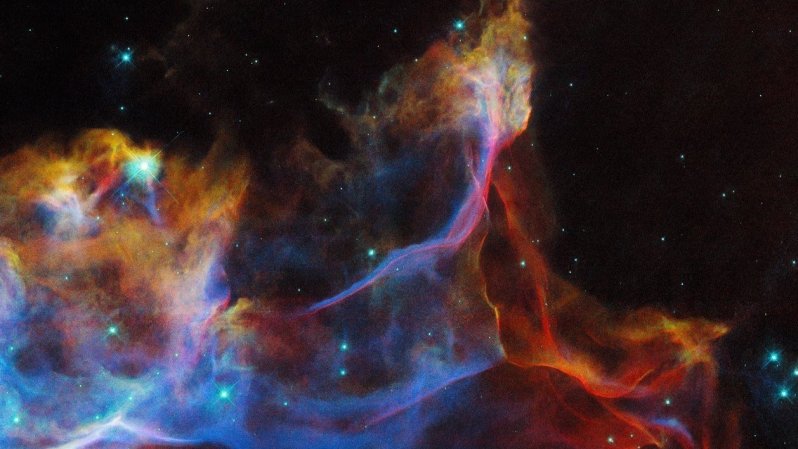 A colorful, glowing nebula that reaches beyond the top and bottom of the image. It is made of translucent clouds of gas: wispy and thin with hard edges in some places, and puffy and opaque in others. Blue, red and yellow colours mix together, showing light emitted by different types of atoms in the hot gas. Bright and pointlike stars are scattered across the nebula. The background is black